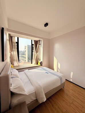 A modern hotel room with a large bed, a window with curtains, and a view of buildings outside. - Elizabeth Golf Apartment (Kigali)