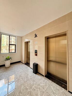 A hallway with two elevators, a potted plant, and a no-smoking sign. - Elizabeth Golf Apartment (Kigali)
