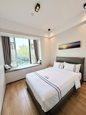 A modern hotel room with a large bed, a window with curtains, a painting on the wall, and a wooden floor. - Elizabeth Golf Apartment (Kigali)