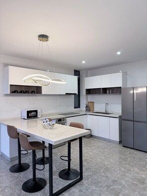 A modern kitchen with a central island, bar stools, a built-in microwave, and a stainless steel refrigerator. - Elizabeth Golf Apartment (Kigali)