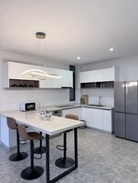 Una cocina moderna con una isla central, taburetes de bar, microondas integrado y un refrigerador de acero inoxidable.