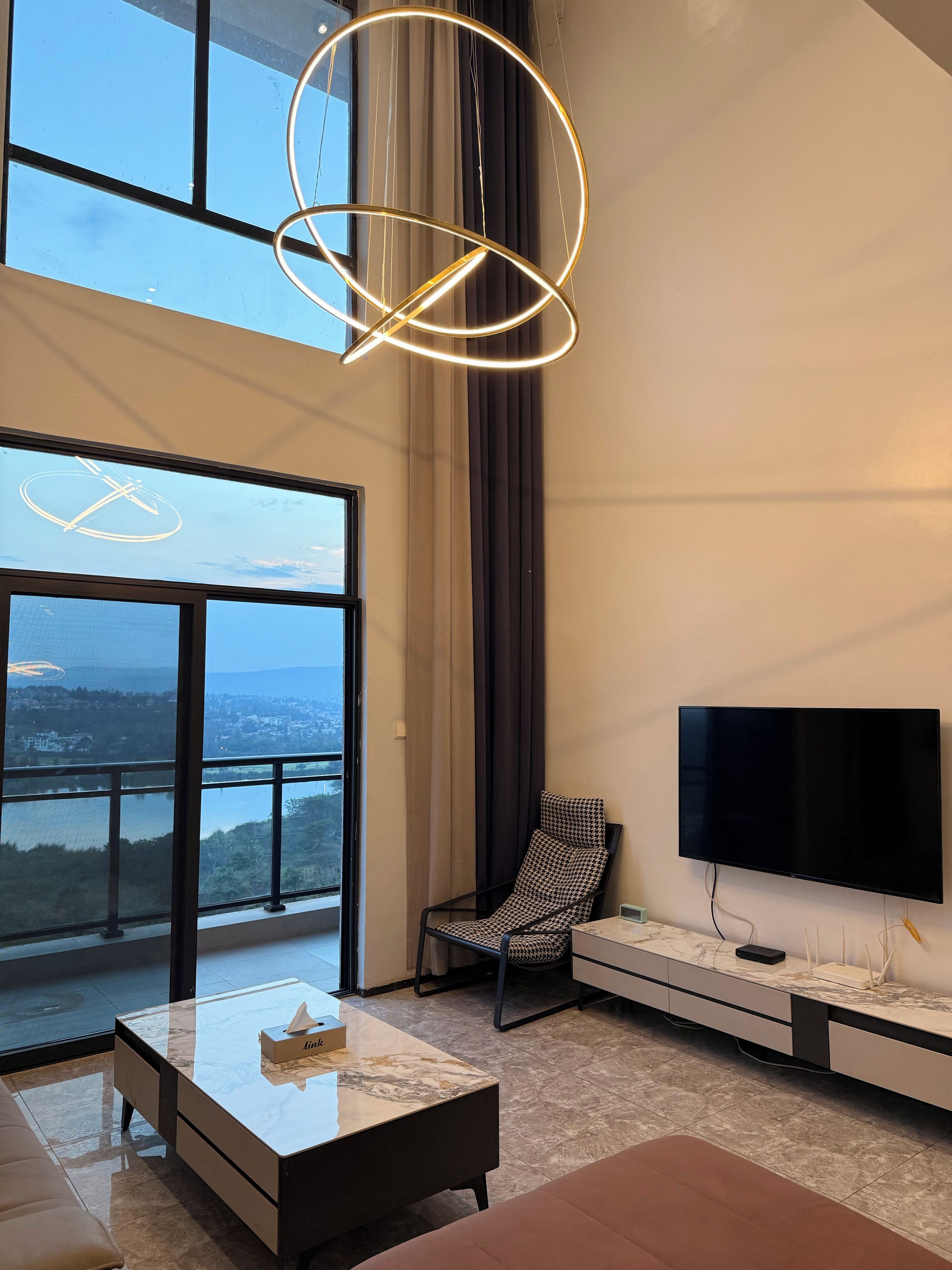 Una sala de estar moderna con un ventanal grande, un televisor de pantalla plana, un sillón estampado y una mesa de centro de mármol.