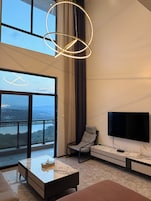 A modern living room with a large window, a flat-screen TV, a patterned armchair, and a marble coffee table.