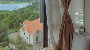 Una habitación con un gran ventanal que ofrece vistas a un lago, vegetación y un pueblo lejano.