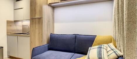 A modern living room with a blue sofa, wooden cabinets, and a kitchen area in the background.