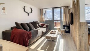 Ein modernes Wohnzimmer mit großem Fenster, einer Couch, einem Couchtisch und einem an einer Holzwand befestigten Fernseher.