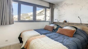 Ein Schlafzimmer mit großem Fenster, einem Bett mit vielen Kissen, einem Holz-Kopfteil und einer Wand mit einer Berggirlande.
