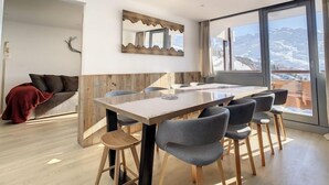 Ein moderner Essbereich mit Holztisch und -stühlen, einer Couch mit roter Decke und einem großen Fenster mit Blick auf die Berge.