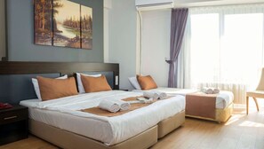 Habitación de hotel con dos camas, un ventanal con cortinas, un cuadro en la pared y una mesita de noche con un control remoto.