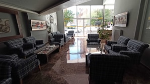 A lobby with plaid furniture, a framed picture, and a large window with a view of the street. - Sinada Otel (Eskisehir)