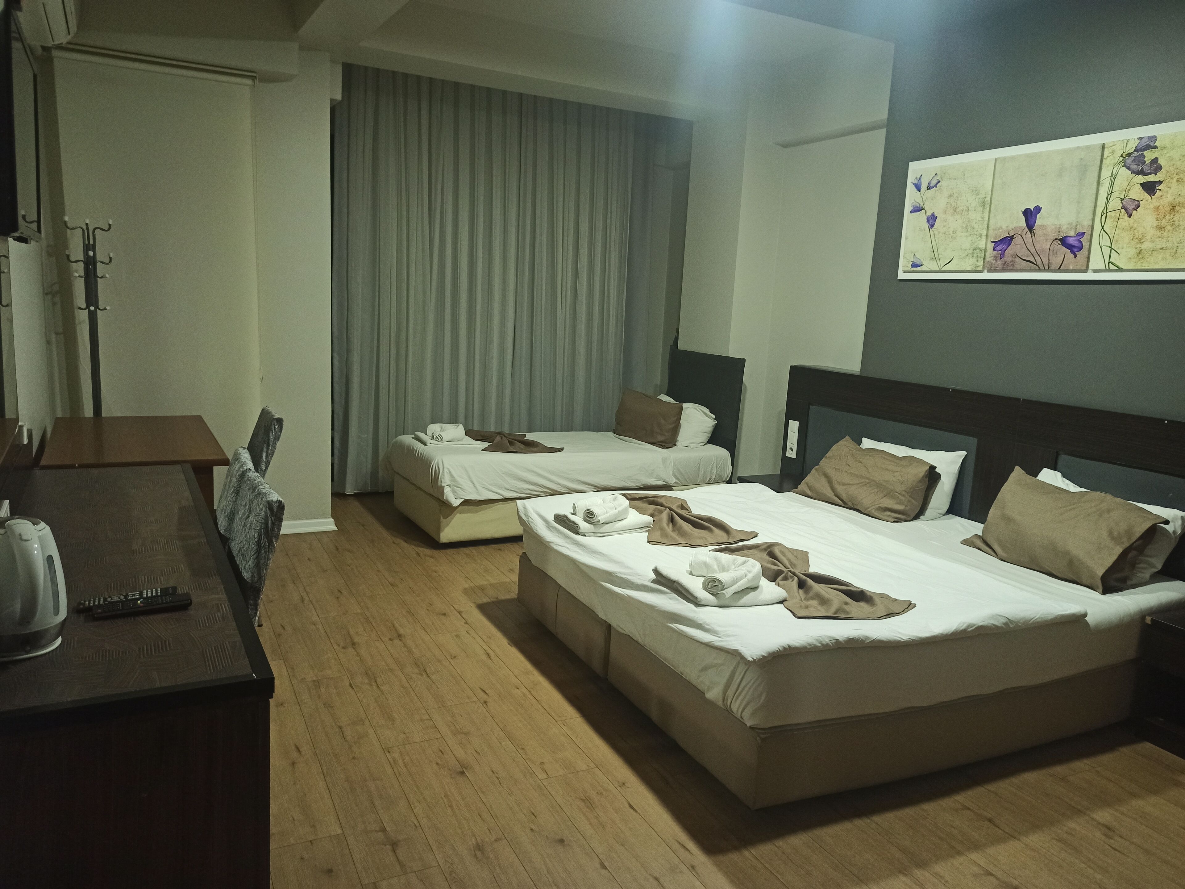 A hotel room with two beds, a desk with a kettle, and a painting on the wall.