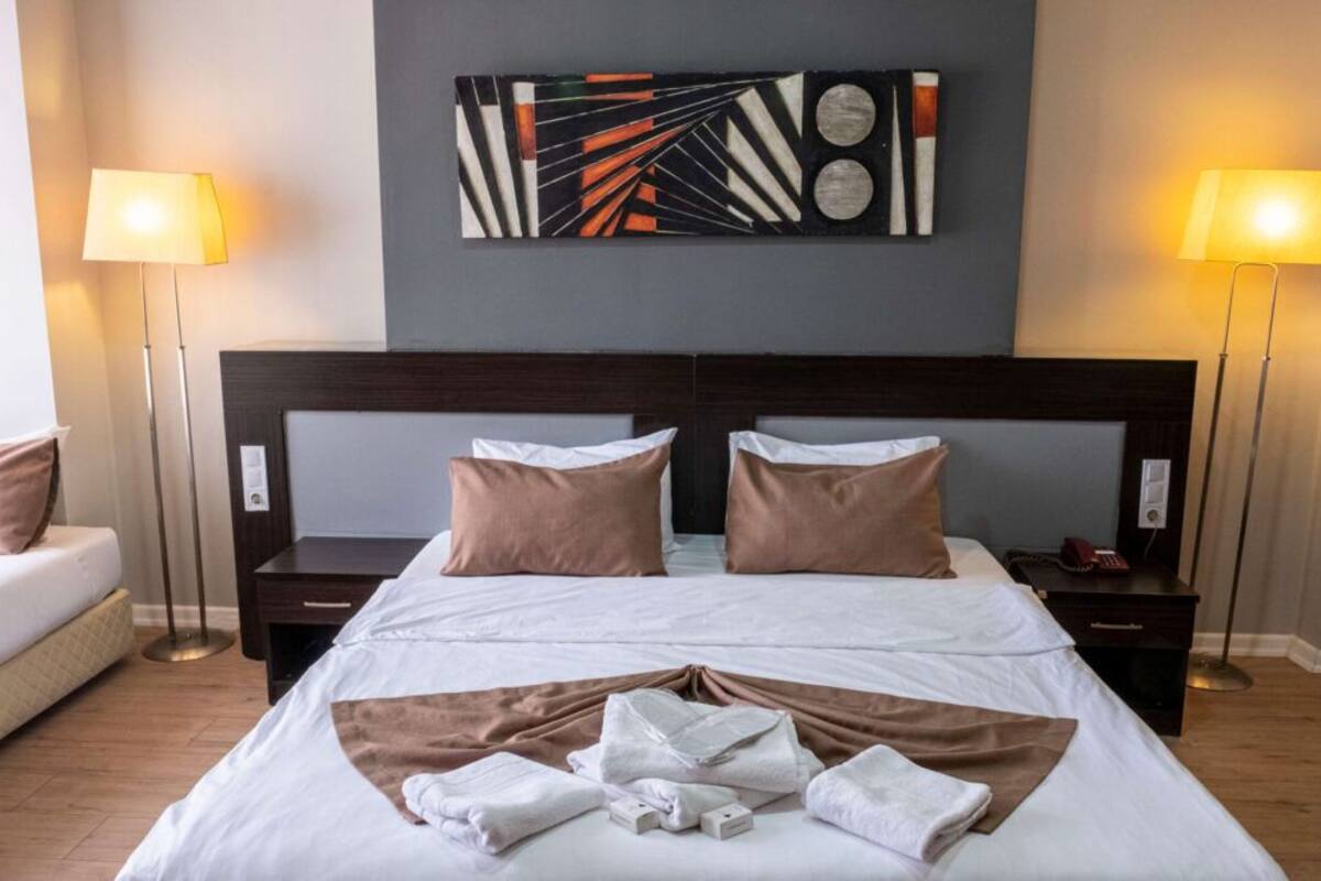 A hotel room with a large bed, two bedside tables, a headboard, and a wall-mounted abstract art piece.