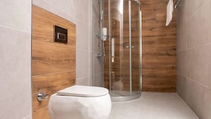 A modern bathroom with a glass shower enclosure, a toilet, and wooden wall panels. - Sinada Otel (Eskisehir)