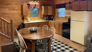 Ein Holzblockhaus-Innenraum mit Küche und Essbereich, ausgestattet mit Holzsärchen, einem Herd, einem Kühlschrank und einem karierten Boden.