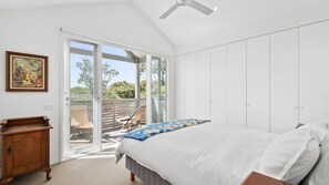 Ein Schlafzimmer mit einem Bett, einer Holzkommode, einem Gemälde und einer Glastür, die auf einen Balkon mit Stühlen führt.