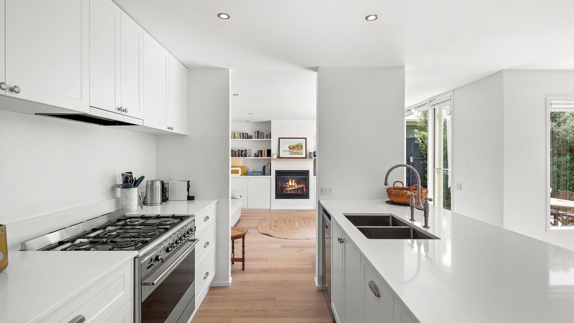 Eine moderne Küche mit weißen Schränken, einem Gasherd und einem eingebauten Backofen. Es gibt eine Essecke mit einem Holztisch und Stühlen sowie einen Kamin.