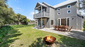 Ein zweistöckiges Haus mit überdachter Terrasse und Feuerstelle im Garten.