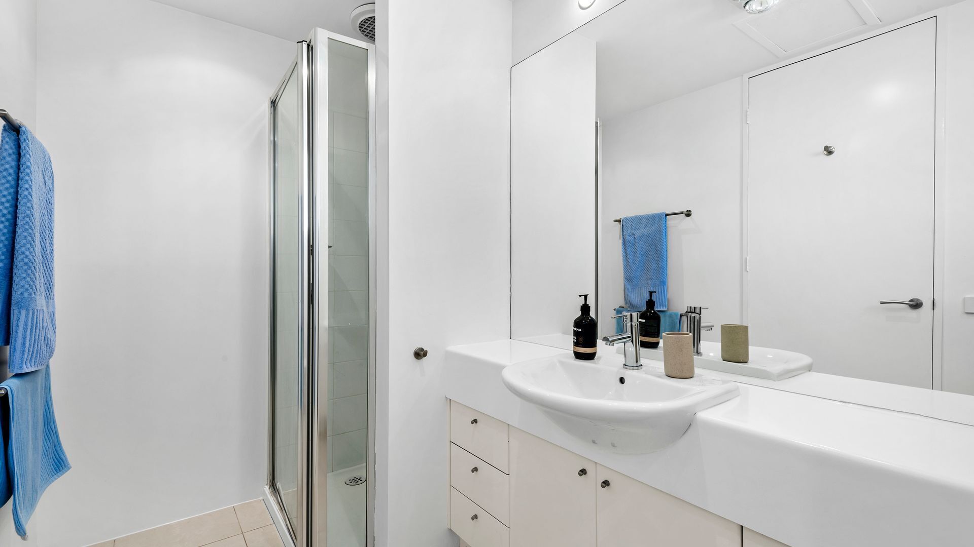 A modern bathroom with a glass shower enclosure, a white sink with a mirror above it, and a towel rack with a blue towel.