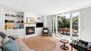 Uma sala de estar moderna com lareira, um sofá, uma mesa de centro e um espaço de jantar com assentos externos.