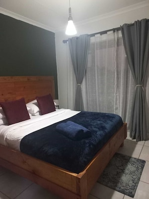 Un lit avec une tête de lit en bois, du linge de lit blanc et une couverture bleue.