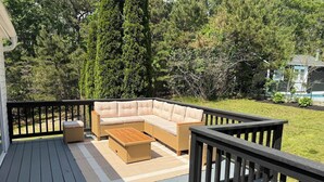A deck with a sectional sofa and a coffee table, surrounded by a wooden railing.