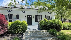 A two-story house with a front porch, a black door, and a staircase leading to the entrance.