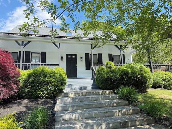 A two-story house with a front porch, a black door, and a staircase leading to the entrance.