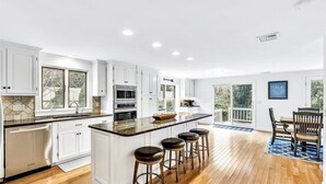 A modern kitchen with white cabinets, a large island with stools, and a wooden floor.