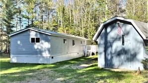 A mobile home with a porch and a small shed with an American flag. - Tree Top Retreat on the Peaceful Flambeau River! (Park Falls)