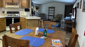 A kitchen with wooden cabinets, a stove, microwave, and a dining area with blue placemats and chairs. - Tree Top Retreat on the Peaceful Flambeau River! (Park Falls)