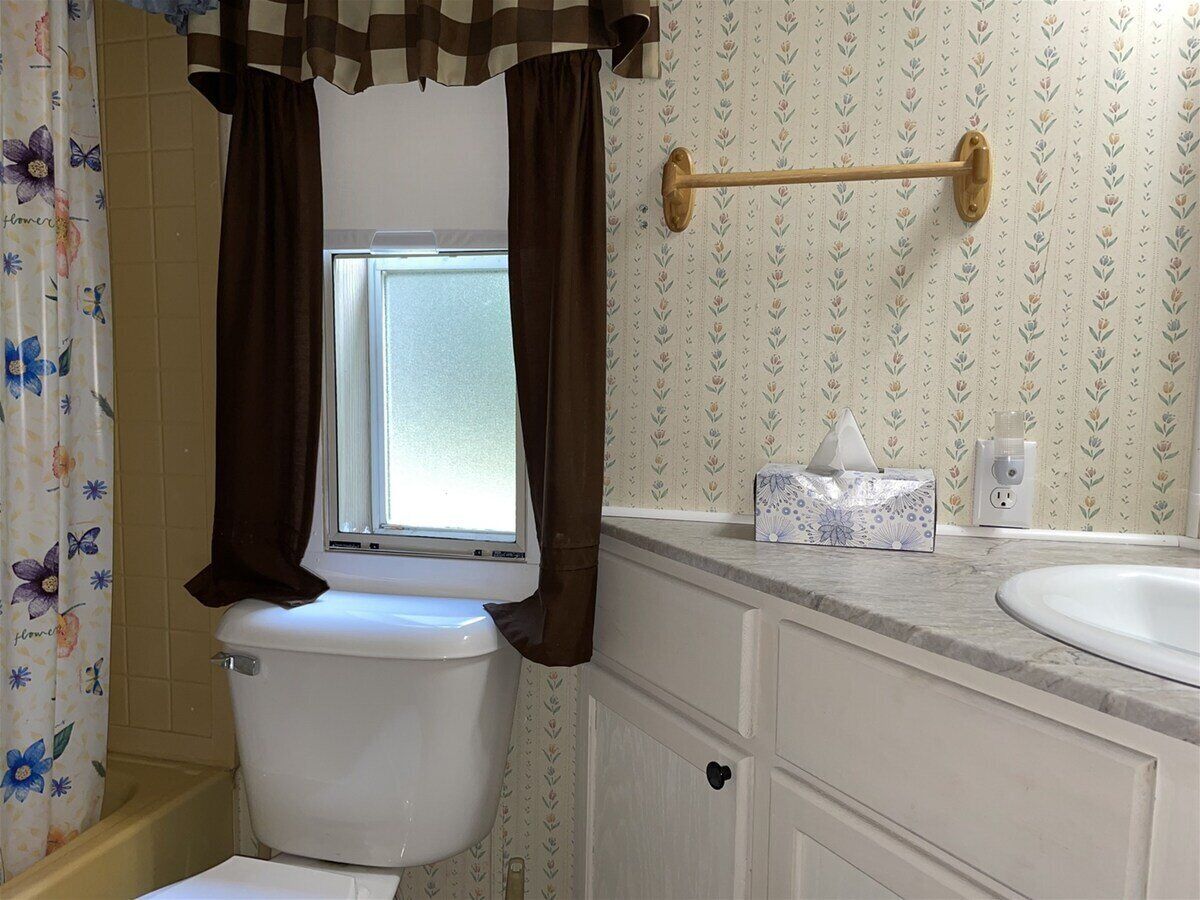 A bathroom with a toilet, a window with curtains, a towel rack, a tissue box, and a sink.