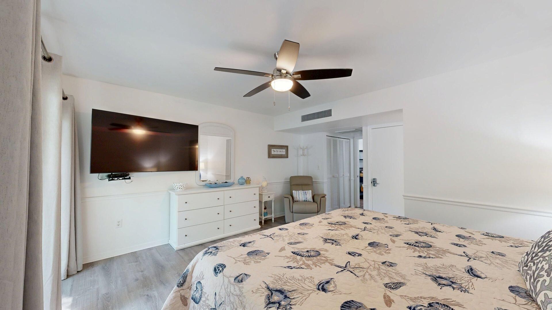 Une chambre à coucher comprenant un lit, un ventilateur de plafond, une commode, une chaise et un téléviseur.