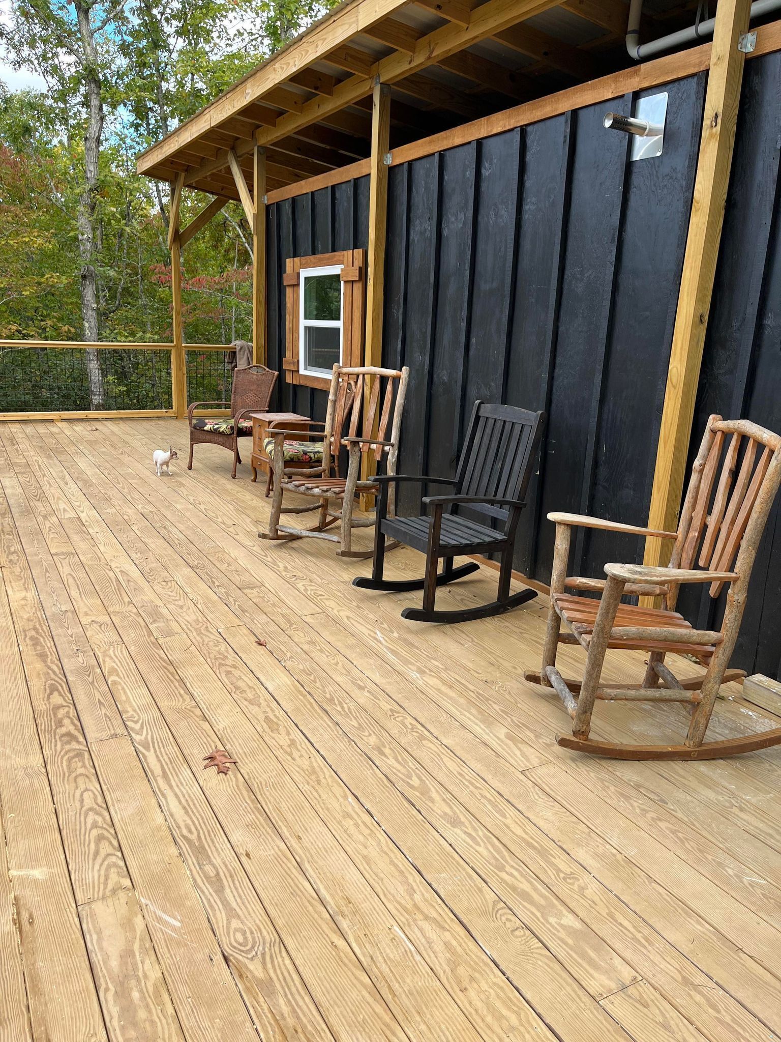 Une terrasse en bois avec quatre fauteuils à bascule et une petite table, donnant sur une zone boisée.