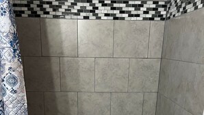 A bathroom with a bathtub, grey tiled walls, and a patterned shower curtain.