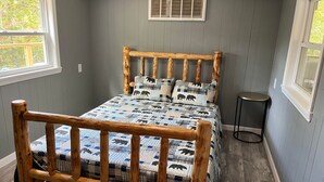 A wooden bed with a checkered blanket, a small bedside table, and a window with blinds.