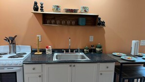 A kitchen with a stove, sink, and countertop. There are decorative items on the shelf above the sink and a small table with plates.