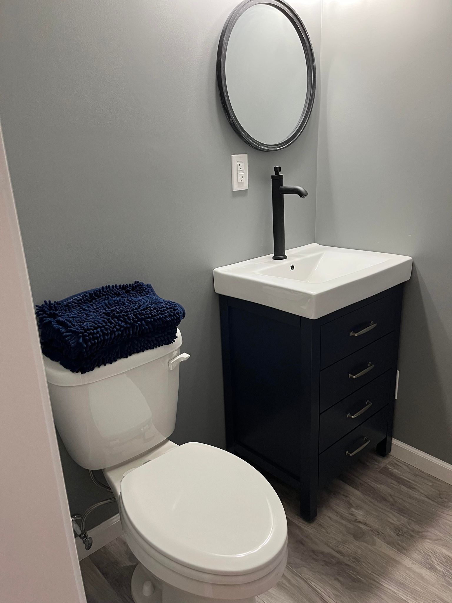 Un bagno con un water bianco, un lavandino nero e un armadietto scuro.