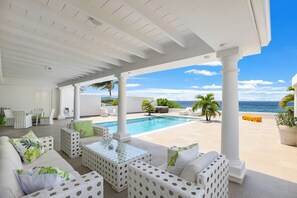 Un espace extérieur abrité avec une piscine, des meubles blancs et une vue sur l’océan.