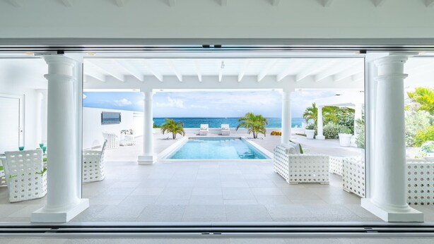 Un área de piscina moderna con vistas al mar, columnas blancas y sillas de descanso.