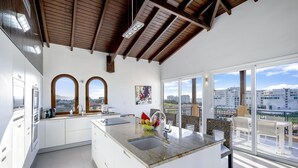 Una cocina moderna con una isla central, armarios blancos y ventanas amplias que ofrecen vistas a la ciudad.