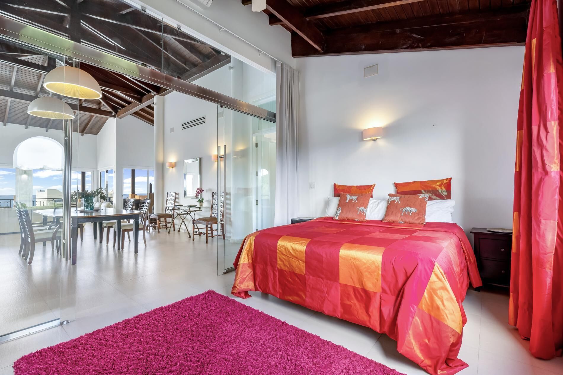 A modern bedroom with a large bed, a dining area with chairs, and a view of the outdoors.