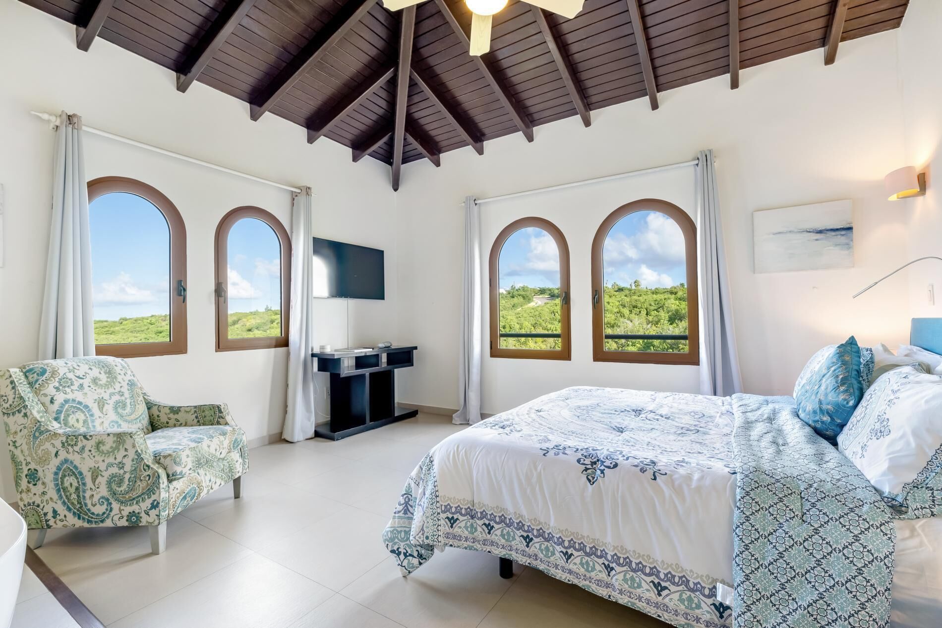 A bedroom with a bed, a desk, a chair, and two windows with arched tops.