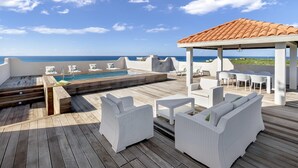 Una terraza en la azotea con piscina, mobiliario de mimbre blanco y vistas al océano.