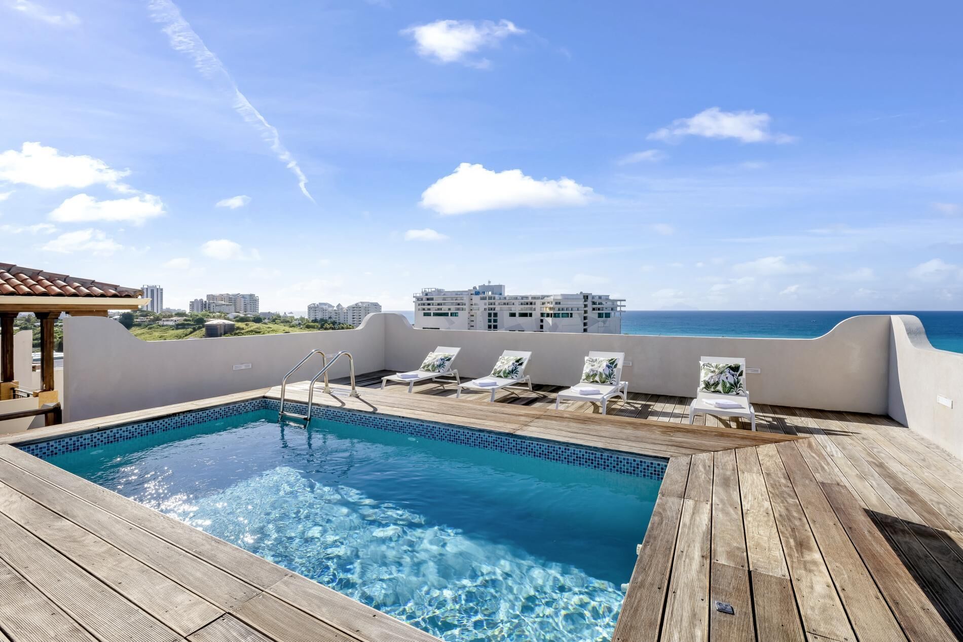 A rooftop pool with clear blue water, surrounded by wooden deck and lounge chairs.