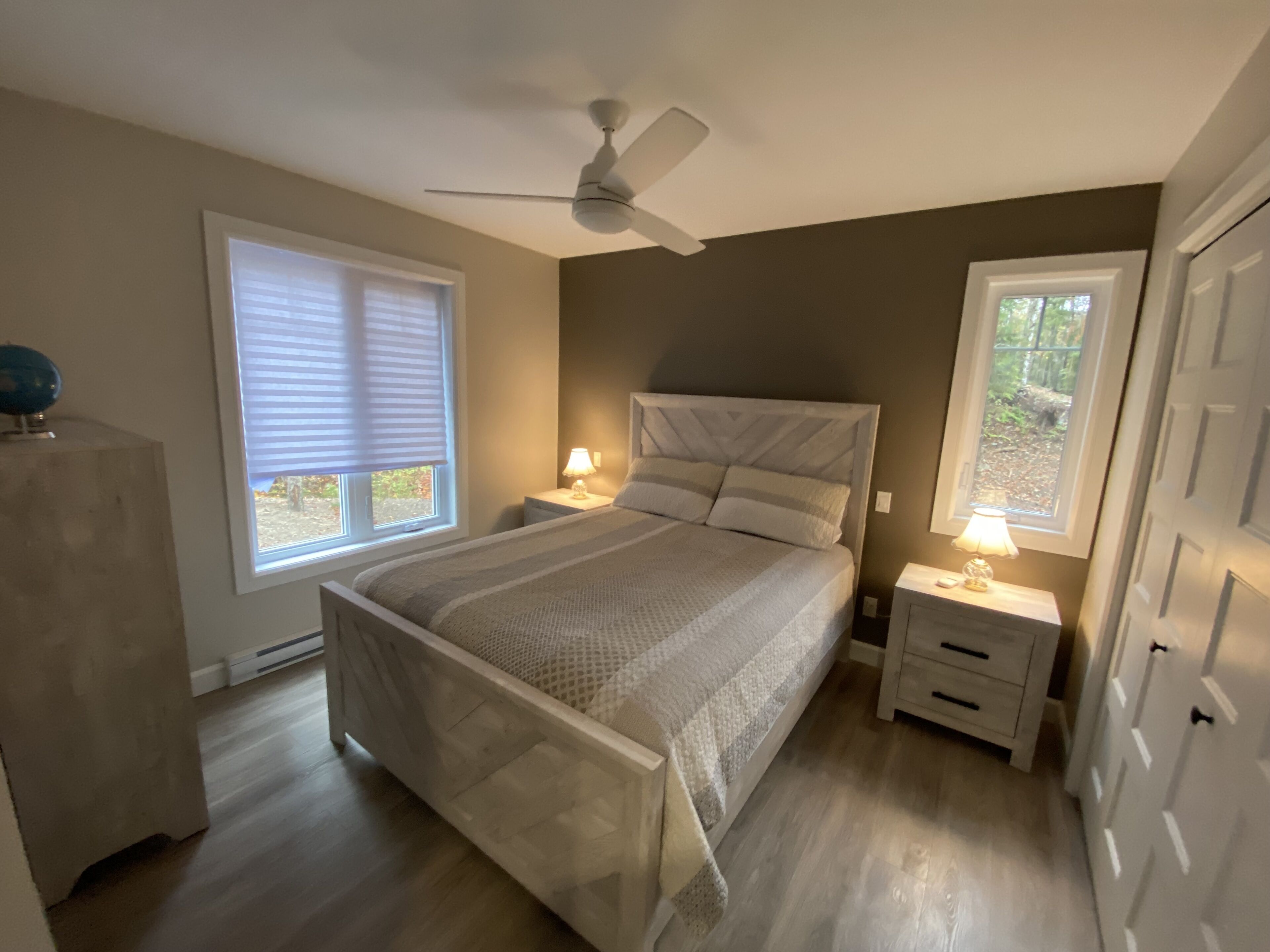 Une chambre à coucher avec un lit, des tables de chevet, un ventilateur de plafond et une fenêtre.