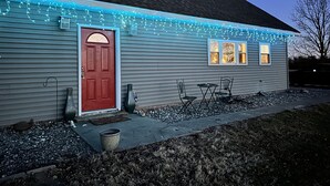 A house with a red door, a small porch with chairs, and string lights along the roof.