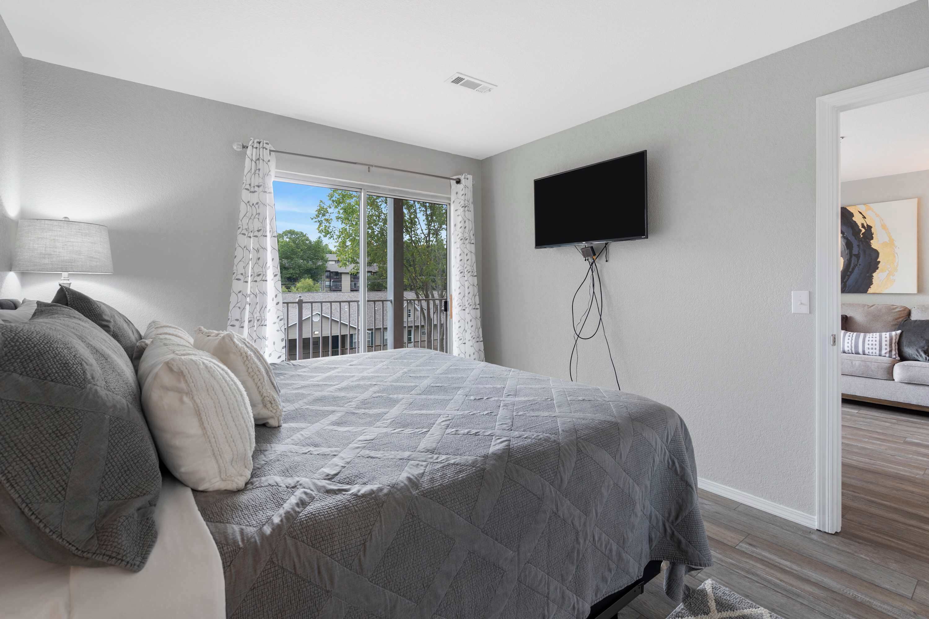 Une chambre avec un grand lit, un téléviseur fixé au mur et un balcon agrémenté de rideaux.