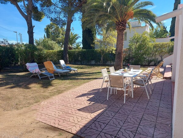 An outdoor patio with lounge chairs and a dining table, surrounded by trees and a building in the background. - Magnificent wooded villa, ideally located close to the beach. (L'Escala)