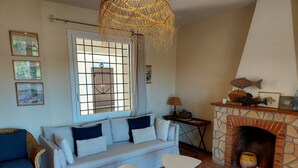 Ein Wohnzimmer mit Kamin aus Stein, einer Couch mit Kissen, einem Korbsessel und einem kleinen Tisch.
