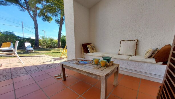 Eine Terrasse mit einem Holztisch, einem weißen Sofa mit Kissen und einem gelben Stuhl.